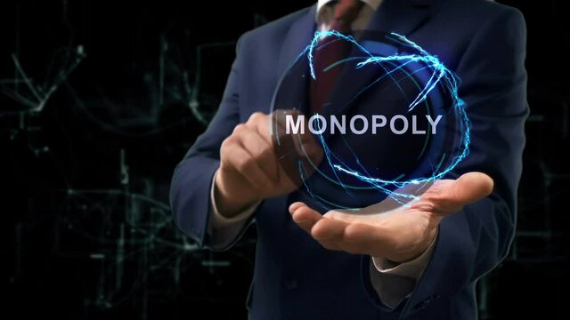 Businessman shows concept hologram text Monopoly on his hand. Man in business suit with future technology screen and modern cosmic background