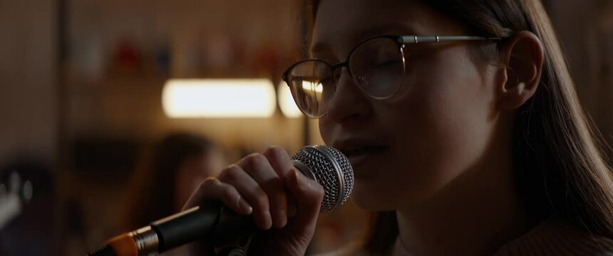 CU Portrait of Caucasian teenager girl wearing glasses singing during rehearsal with her band inside home garage. Shot with 2x anamorphic lens