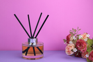 aroma scent reed diffuser glass bottles decorate display on the purple table with bouquet of roses with background of pink cement wall in the living room on valentine day