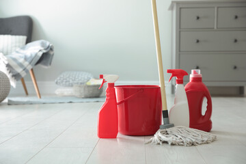 Bucket, mop and different cleaning products on floor indoors. Space for text