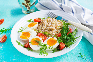 Breakfast oatmeal porridge with boiled egg, cherry tomatoes and arugula. Healthy balanced food.