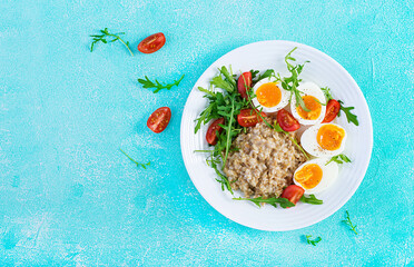 Breakfast oatmeal porridge with boiled egg, cherry tomatoes and arugula. Healthy balanced food. Top view, above, copy space
