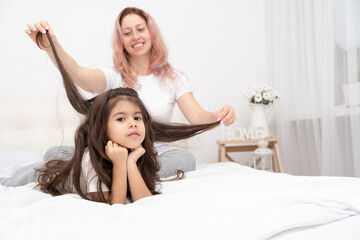 mother play with little active daughter in bed at home, having fun, activity with children