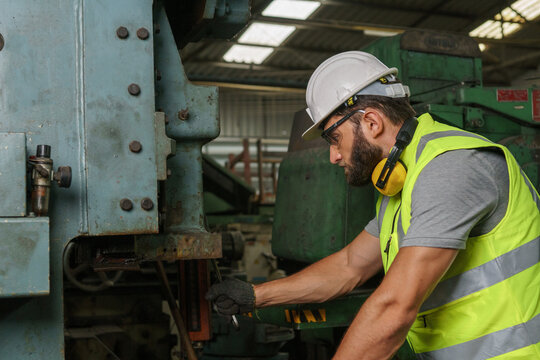 Industrial engineer in hard Hat wearing safety . He looking of works at Industry manufacturing factory. In the background welding / metalworking processes are in progress.