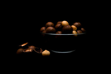 Shelled and unshelled macadamia nuts in glass bowl on dark background