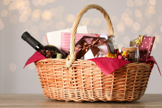 Wicker basket with gifts, wine and food against blurred festive lights. Space for text