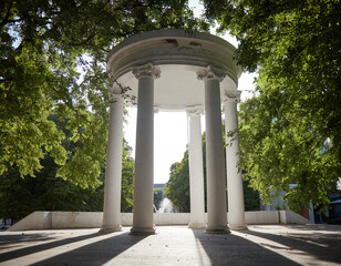 White stone gazebo with a round roof in the park view from below opposite the sun