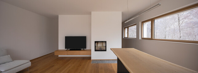 Wooden table with design lamp, fireplace, tv and window to the forest of the Swiss Alps