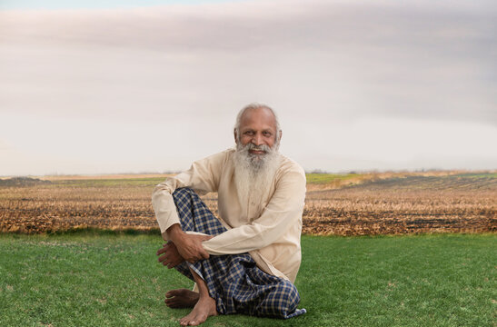 A HAPPY OLD MAN SITTING ON GRASS WITH FARMLAND IN BACKGROUND	