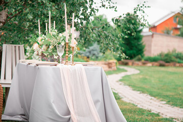 A festive wedding table with candles, glasses, decorated with flowers. The decor is made in orange and green tones. Close up. On the plates are guest lists and wishes.