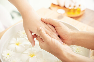 Obraz na płótnie Canvas Beautician massaging hand of female spa salon client. Spa treatment and product for female feet and hand spa. white flowers in ceramic bowl with water for aromatherapy at spa.