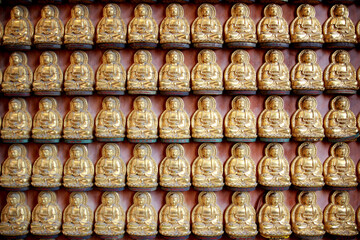 Naklejka premium Numerous golden Buddha statues are placed neatly on the wall.