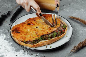 female hands with a knife and a fork cut Khachapuri with lamb and chili. Georgian national food