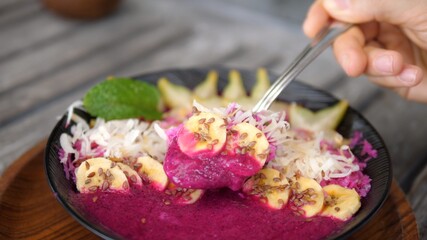 Obraz na płótnie Canvas Spoon dips into tropical smoothie bowl showing it to the camera. Healthy organic vegan breakfast option