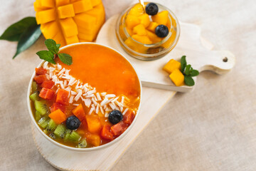 Fresh fruit breakfast. Smoothie bowl of mango, papaya on the table, decorated with pieces of kiwi, blueberry berries and mint leaf