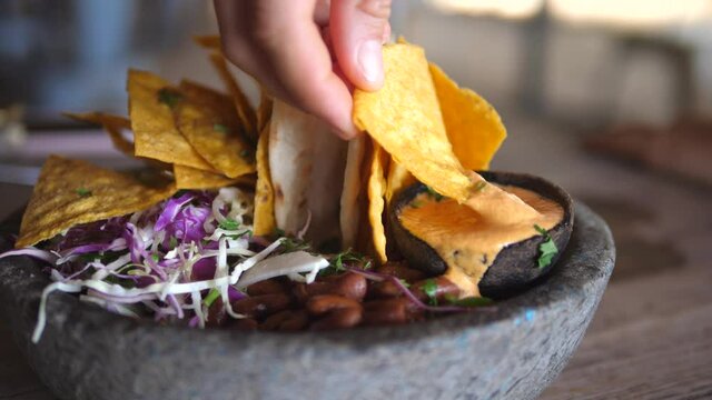 Hand dipping nacho in vegan creamy sous. Healthy vegan Mexican bowl with salsa, beans and dips