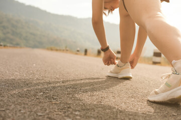 woman tying knots shoe laces,on empty road,in morning