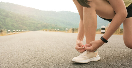 woman tying knots shoe laces,on empty road,in morning