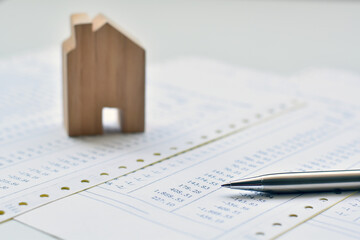 Stainless steel pen tip on documents pile with wooden blurred model house is background.