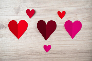 Cutted and folded paper Red hearts on a bright wooden Background. Card for Valentine's Day.