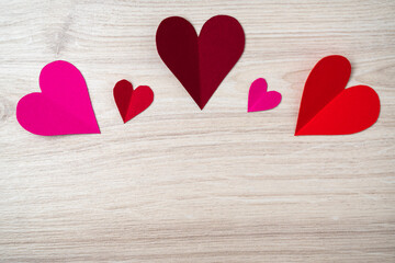 Cutted and folded paper Red hearts on a bright wooden Background. Card for Valentine's Day.