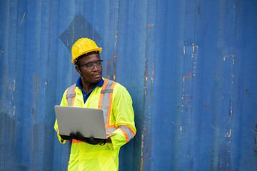 worker man in protective safety jumpsuit uniform with yellow hardhat and use laptop check container at cargo shipping warehouse. transportation import,export logistic industrial service