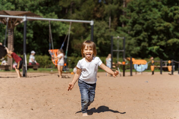 cute emotional little girl 3 years old posing and laughing on the playground on a summer sunny day