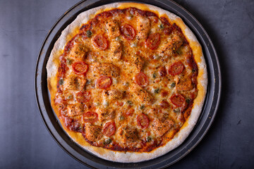 Pizza with salmon, tomatoes and capers. Whole pizza on a black background. Close-up, top view.