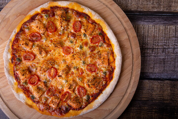 Pizza with salmon, tomatoes and capers on a wooden board. Whole pizza. Close-up, top view.