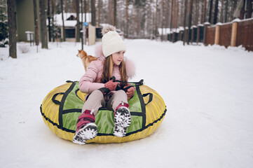 Little cute girl in pink warm outwear having fun rides inflatable snow tube in snowy white cold winter outdoors. Family sport vacation activities.