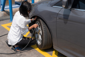 Woman driver checking air pressure and filling air in cars tires. 