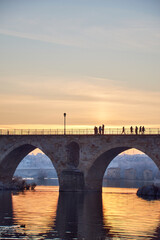 Fototapeta premium People walking on a stone bridge at sunset and the frozen trees in winter at the golden hour
