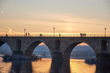 Fototapeta na wymiar People walking on a stone bridge at sunset and the frozen trees in winter at the golden hour
