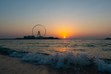 Sunset over the sea view to the Dubai Eye giant Ferris at artificial island Bluewaters Island  close to JBR beach. Amazing sunset on the beach in UAE.