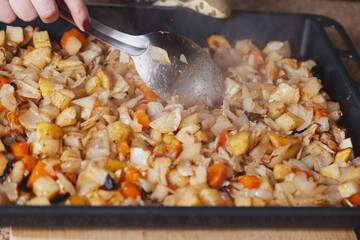 Large spoon stirs stewed vegetables on baking sheet