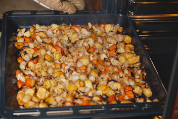 Hands in mittens take out baking tray with vegetables oven