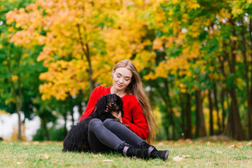 Young attractive woman holding her dachshund dog in her arms outdoors in sunrise in park at autumn