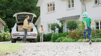 Family unloading boxes from car as they move into new home as son with skateboard runs to help - shot in slow motion - Powered by Adobe