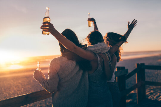 Group of female best friends hugging each other and cheering with drinks