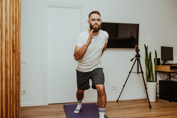 Young man making sport fitness exercises at home. Training during quarantine. Online training in front of the smartphone camera.