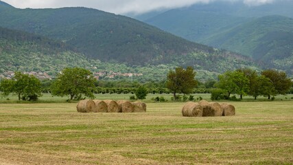 Beautiful landscape, hay roll bales at harvest in green field and hills in dramatic clouds on background. Meadow in valley near Shipka town, Balkan Mountains, Bulgaria. Agriculture and nature concept
