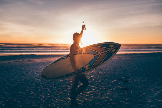Woman with surfboard enoying beer at sunset after she went surfing