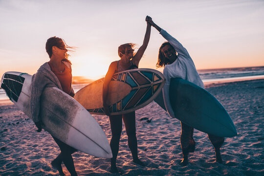 Group of female friends with surfboards giving each other high fives after surfing