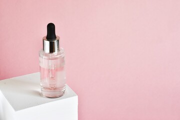 Bottle of moisturizing face oil on a white stand on a pink background. A professional product for a perfect complexion. Women's accessories, cosmetic base. Copy space.