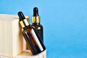 Glass cosmetic bottles with pipettes on a wooden cube on blue background. Anti-aging formula,...