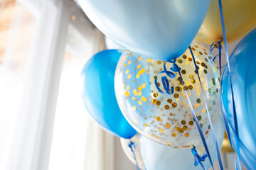 Blue and transparent balloons with golden confetti on the background of a large window. Light interior
