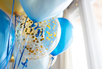 Blue and transparent balloons with golden confetti on the background of a large window. Light interior
