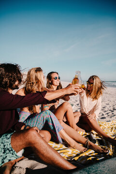 young adult friends cheering with beer bottles at beach on vacation