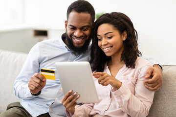 Black couple using tablet and debit credit card at home