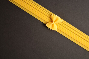 "Raw italian farfale bow pasta piece on spaghetti isolated on dark background. 
Food imitation of Ribbon and bow "
